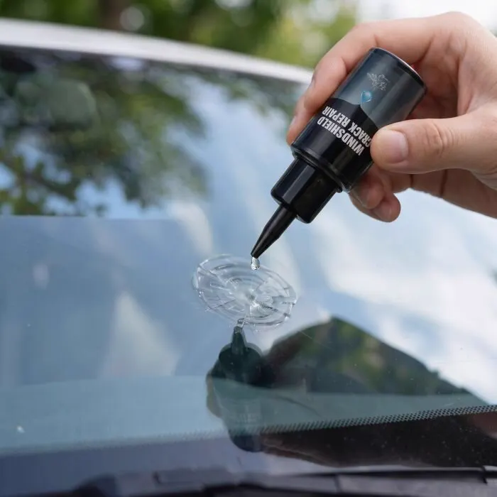 Hand applying a drop of Glasyx resin onto a star chip in a car windshield